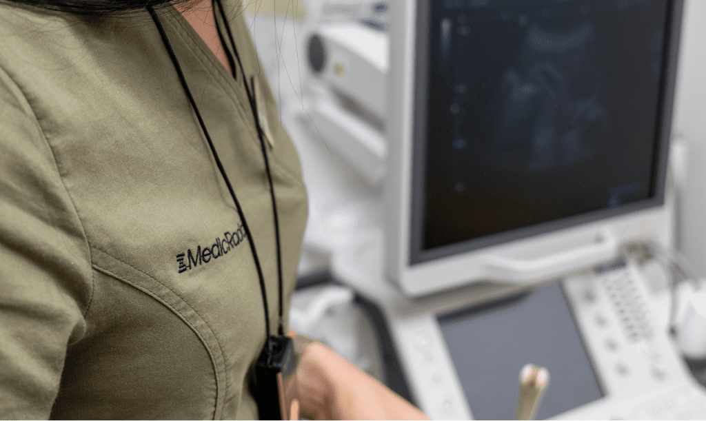 Medicinska sestra u uniformi sa logom Medicrad ispred dijagnostičke opreme, spremna za sistematski pregled.